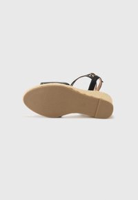Black sandal with a woven sole, featuring a textured rubber sole and an ankle strap. The footbed has a smooth finish.