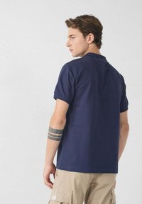 Marineblauw polo shirt met kraag en korte mouwen, gemaakt van een soepele stof. De achterkant heeft een klein accent bij de hals.
