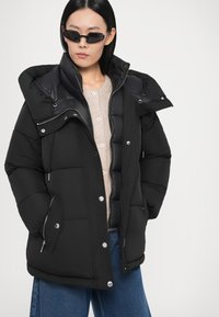 Must ploomjas kõrge krae, tõmblukk ja nööpidega kinnitused, küljetaskud ning veidi läikiv viimistlus. Vabaaja lõige ja struktureeritud disain.