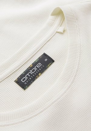 Close-up of a white textured shirt collar with a black "ombre QUINTESSENCE" brand label showing size M.
