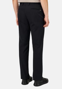 Juodi kelnės su tiesiomis kojomis, turinčios galinę kišenę ir subtilų siuvinėjimą. Pora su juodais sportiniais batais.