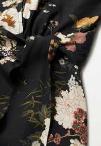 Tejido negro con un patrón floral en tonos de crema, rosa y oro, que presenta un detalle de lazo y una textura suave y fluida.