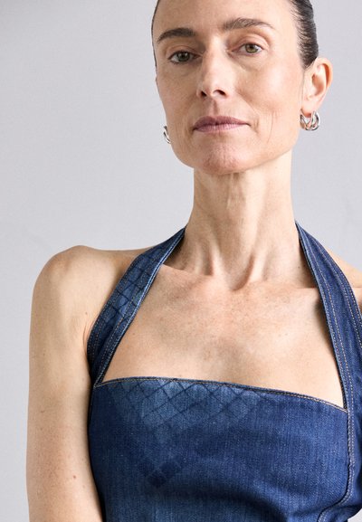 Plavi traper halter top s kvadratnim izrezom i širokim trakama. Ima suptilan dijamantni uzorak i vidljive šavove.