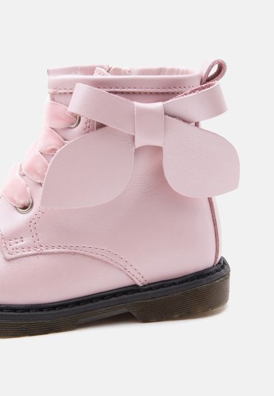 Botte enfant rose clair avec un grand nœud en cuir sur le côté et une semelle en caoutchouc noire.