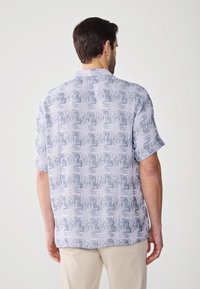 Camisa de manga corta en azul claro con un patrón abstracto texturizado. Presenta un cuello y un dobladillo recto. El material parece ligero.