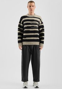 Gestreepte wollen trui in beige en marineblauw, met een ronde hals en een losse pasvorm, gecombineerd met zwarte slim fit broek en lichte sportschoenen.