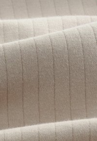 Lysbeige ribbet stof med en blød tekstur, der har jævnt fordelt lodrette striber. Glat, strikket materiale med subtile fibre.