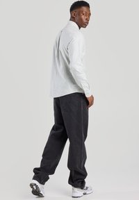 Camisa de rayas de manga larga en azul claro y blanco, combinada con jeans de mezclilla negros. Modelo vistiendo zapatillas blancas, visto desde la parte de atrás.