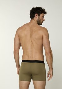 Boxer shorts verde oliva con una cinturilla elástica negra, textura de tela suave y un diseño ajustado, mostrados desde la vista trasera.