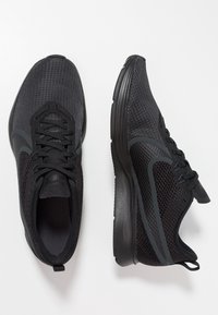 Chaussures de sport noires avec une tige en mesh texturé, une semelle rembourrée et des accents latéraux contrastés. Équipées de lacets et d'une languette à l'arrière.