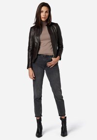 Giubbotto di pelle nera, dolcevita beige, jeans grigi a vita alta e stivali neri alla caviglia. Texture liscia, design aderente e polsini arrotolati.