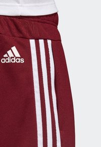 Maroon athletic pants with white side stripes, made of soft fabric, featuring an Adidas logo in white on the left leg.