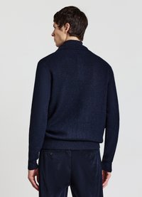 Marineblauer Strickpullover mit hohem Kragen und gerippten Bündchen. Weiche Textur und tailliertes Design. Kombiniert mit passenden marineblauen Hosen.