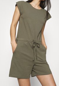 Olivgrön kortärmad jumpsuit med rund halsringning, dragsko i midjan och sidofickor. Tillverkad av mjukt, stretchigt tyg.