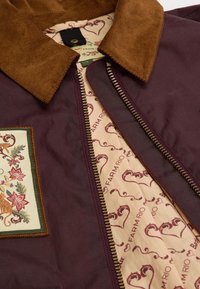 Μπορντό υφασμάτινο μπουφάν με καφέ κοτλέ γιακά, κεντημένο λουλουδάτο μπατζάκι στο στήθος και με σχέδιο εσωτερικής επένδυσης που περιλαμβάνει το κείμενο "FARM RIO".