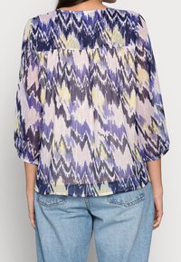Blusa leggera plissettata in un motivo ikat viola, giallo e rosa. Presenta maniche a tre quarti e un orlo curvo.