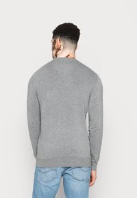 Grijze lange mouwen trui met een ronde hals, gemaakt van zacht materiaal, met ribgebreide boorden en zoom, gedragen met lichtblauwe jeans.