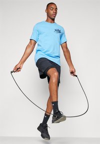 T-shirt Nike azzurro con logo nero, abbinato a pantaloni corti neri. Scarpe da ginnastica nere e calze con logo Nike bianco. Corda per saltare in mano.