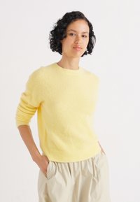 Yellow knitted sweater with a round neckline and ribbed cuffs, paired with light beige, loosely fitted pants. Soft texture and casual design.