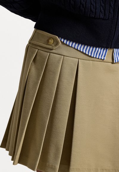 Khaki pleated seelik külgbuttoni detailiga ja sinise ja valge triibulise särgi nähtav tukk. Kanga tekstuur on sile.