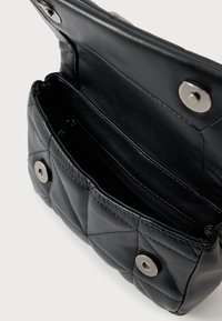 Μαύρη δερμάτινη τσάντα με καπιτονέ σχέδιο, επάνω καπάκι, ασημένιες μεταλλικές λεπτομέρειες και εσωτερική τσέπη με φερμουάρ. Συμπαγής σχεδίαση, λεία υφή και δομημένο σχήμα.