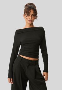 Czarny, prążkowany top typu off-the-shoulder z długimi rękawami i kr�ótkim fasonem, zestawiony z czarnymi spodniami o wysokim stanie z guzikami.