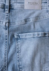 Jeans de mezclilla en azul claro con un diseño clásico de cinco bolsillos, costuras visibles y una etiqueta que dice "Street One".