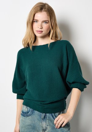 Maglione verde con texture, collo a barca ampio, maniche a palloncino e vestibilità comoda. Abbinato a pantaloni shorts in denim azzurro.