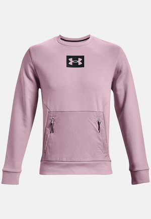 Lys rosa sweatshirt med et sort firkantet logo på brystet, lynlåslommer på forsiden, og ribbede manchetter og kant.