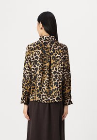 Leopard print blouse in silky fabric, featuring a collar and buttoned cuffs. Black, brown, and gold hues create a bold pattern.