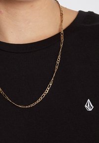 T-shirt en coton noir avec un col rond, arborant un petit logo blanc, assorti à un collier en chaîne dorée fin avec des maillons.