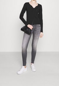 Musta pitkähihainen paita, jossa V-pääntie, yhdistettynä harmaa slim-fit farkkuihin ja valkoisiin tennareihin. Asusteina pieni musta käsilaukku.