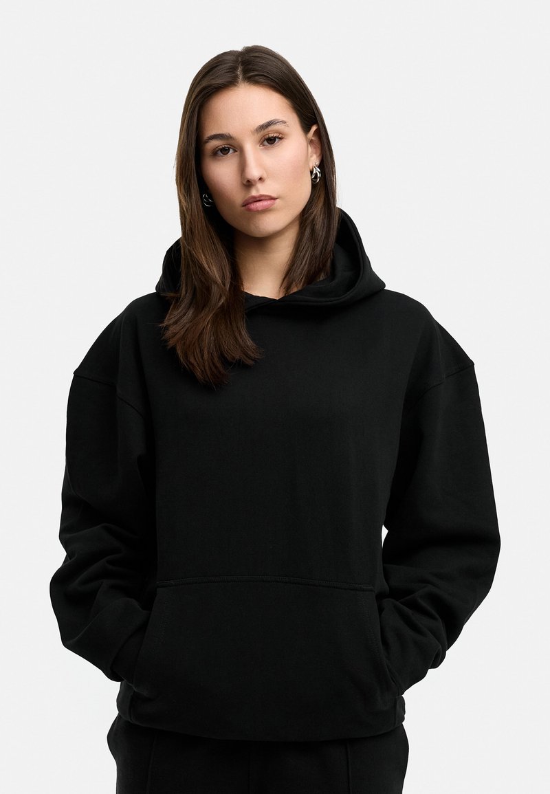 Schwarzer Pullover-Hoodie aus weicher Stoff, mit großer Kapuze, Fronttasche und lässiger Passform. Texturierte Oberfläche mit einfachen Nähten.