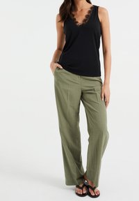 Svart ärmlös topp med spetsdetaljer vid halsringningen, kombinerad med löst sittande olivgröna byxor och svarta platta sandaler.