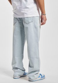 Jeans de mezclilla de corte holgado en azul claro con un acabado desgastado, que cuentan con bolsillos traseros y un diseño de pierna recta, combinados con zapatillas azules.