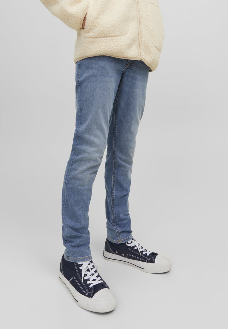 Jean slim bleu clair, en denim avec une finition décolorée, associés à des baskets en toile bleu marine avec des semelles et des lacets blancs.