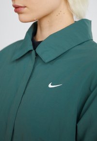 Zöld, könnyű dzseki nagy gallérral és fehér Nike pipa logóval a mellkason. Simító tapintású és egyszerű dizájn.