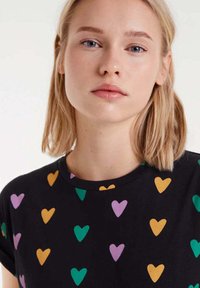 Camiseta negra con patrones de corazones multicolores en amarillo, verde y morado. Mangas cortas, diseño de cuello redondo. Material de algodón suave.
