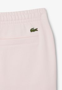 Pantaloni della tuta rosa realizzati in tessuto morbido, con fascia elastica in vita e tasca posteriore con un discreto logo di coccodrillo verde.