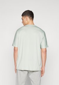 Camiseta verde claro de manga corta con cuello redondo y corte relajado. Textura suave, color sólido y detalles de costura visibles.
