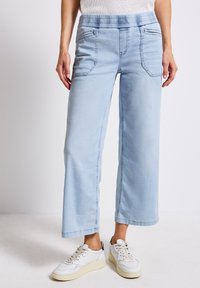 Jean large bleu clair avec une taille élastique, deux poches avant, tissu texturé et coutures sur les bords.