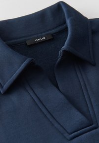 Polo en tricot bleu marine avec un col plat, présentant un tissu texturé et un design minimaliste. L'étiquette indique "OPUS" près de l'encolure.