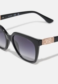 Black square sunglasses featuring gradient lenses from dark to light. Rose gold accent on temples with a geometric pattern near the logo.