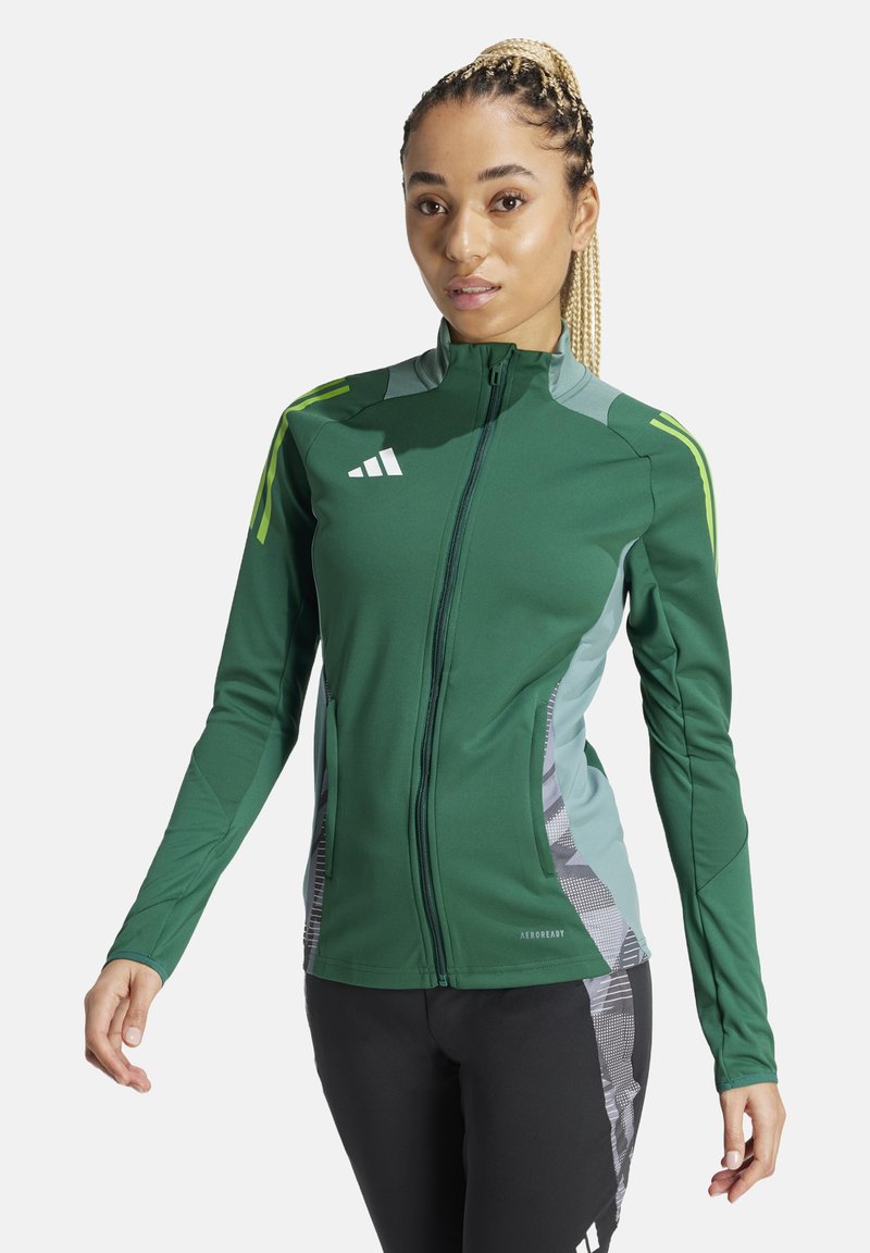 Grüne Sportjacke mit Reißverschlüssen und kontrastierenden hellgrünen und grauen Einsätzen. Verfügt über dezente geometrische Muster und Logo-Akzente auf der Brust.