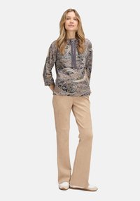 Bluzka z długim rękawem, wzorzysta w odcieniach szarości, beżu i zieleni, z kapturem i sznurkiem do regulacji. W połączeniu z beżowymi, zamszowymi spodniami w stylu dzwon.