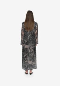 Abito lungo di paillettes argento e nero con taglio dritto, maniche lunghe e spacco laterale. Il design sul retro presenta una cucitura centrale.