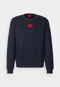 Sweat-shirt bleu marine à col rond avec manches longues et poignets côtelés, avec un petit écusson rouge avec le logo "HUGO" sur la poitrine.
