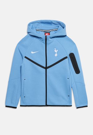 Svetlomodrá mikina Nike na zips s kapucňou, čierny zips a pruhy, logo Tottenham Hotspur na hrudi a vrecko na zips na ľavom rukáve.