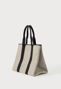 Μπεζ καμβάς τσάντα tote με μαύρες διπλές λαβές και κατακόρυφες μαύρες ράβδους, ορθογώνια βάση και χρυσό κουμπί λεπτομέρεια μπροστά.