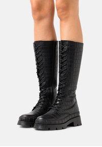 Bottes noires hautes à lacets en cuir embossé effet croco, dotées d'une semelle plateforme épaisse et de motifs texturés le long de la tige supérieure.